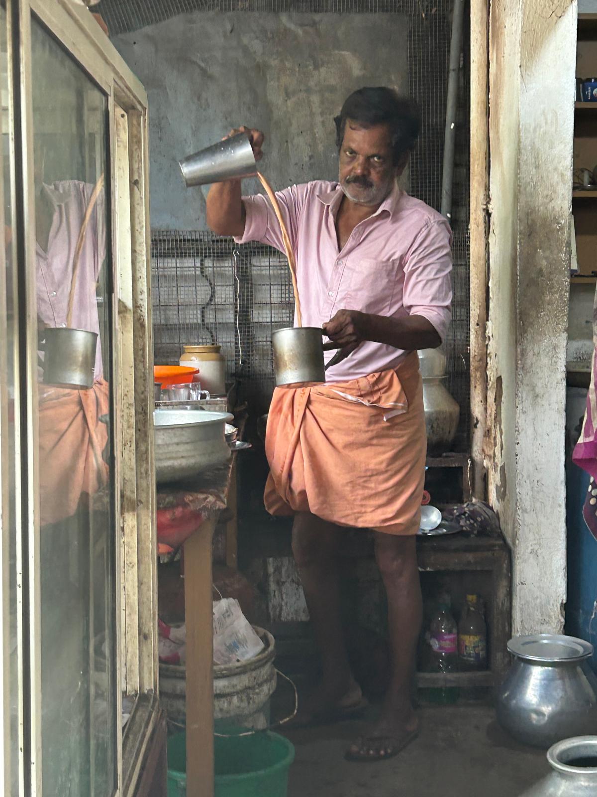 Tea seller pouring chai from a height in a Kerala tea shop