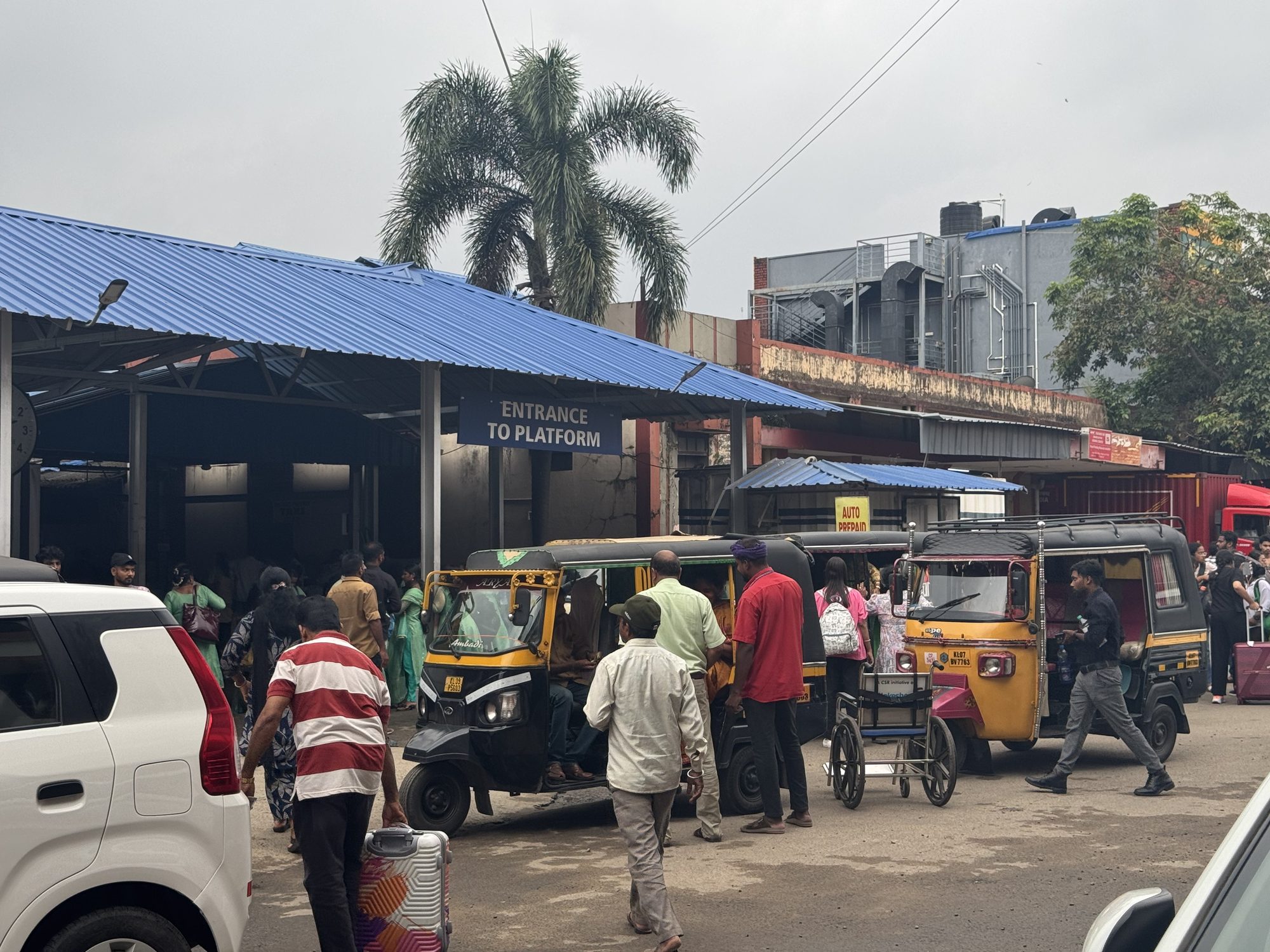 Kerala railway station entrance with auto-rickshaws and passengers heading to the platform